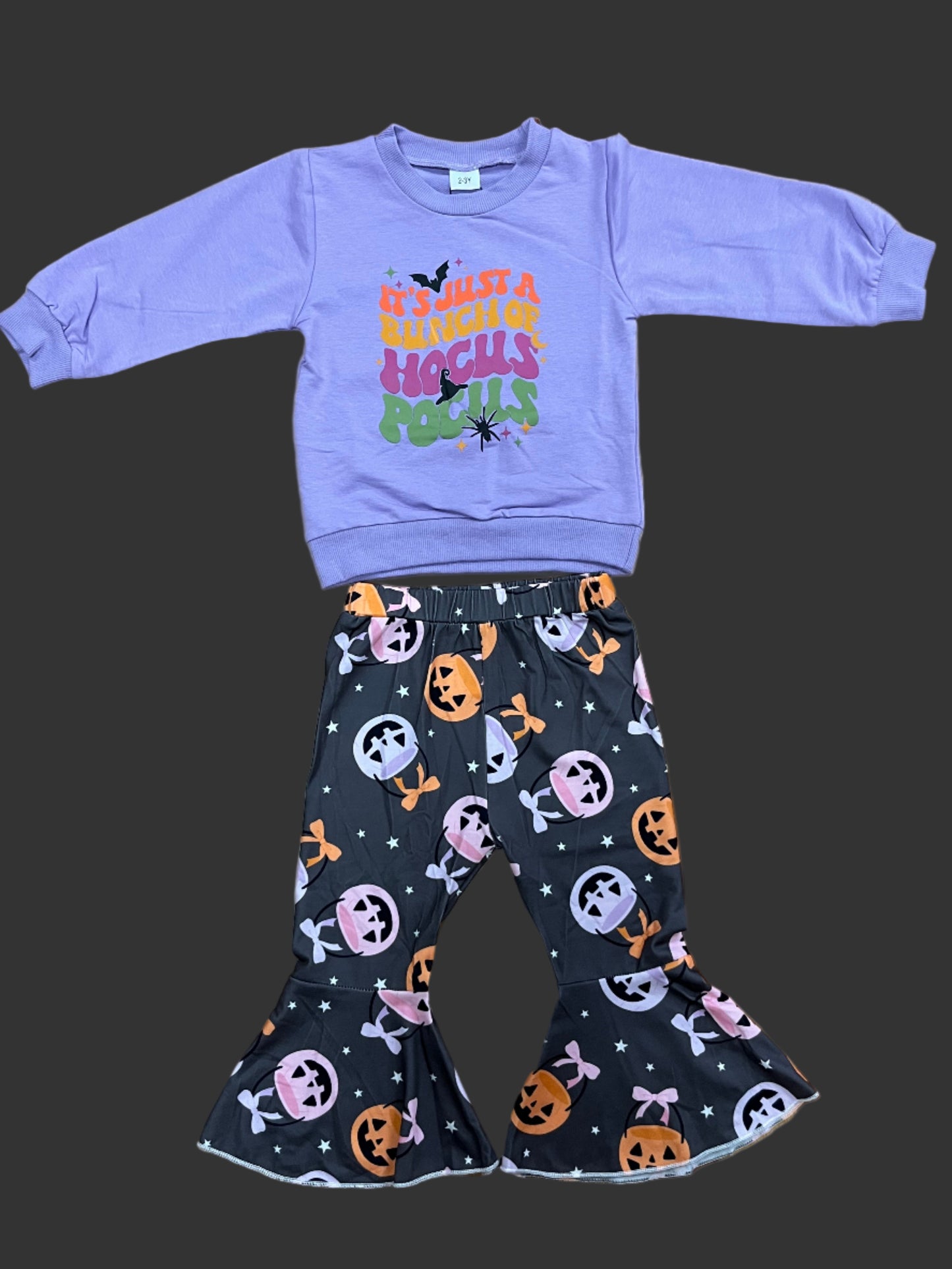 Purple long-sleeve shirt with colorful design and black Halloween-themed pants on a wooden surface