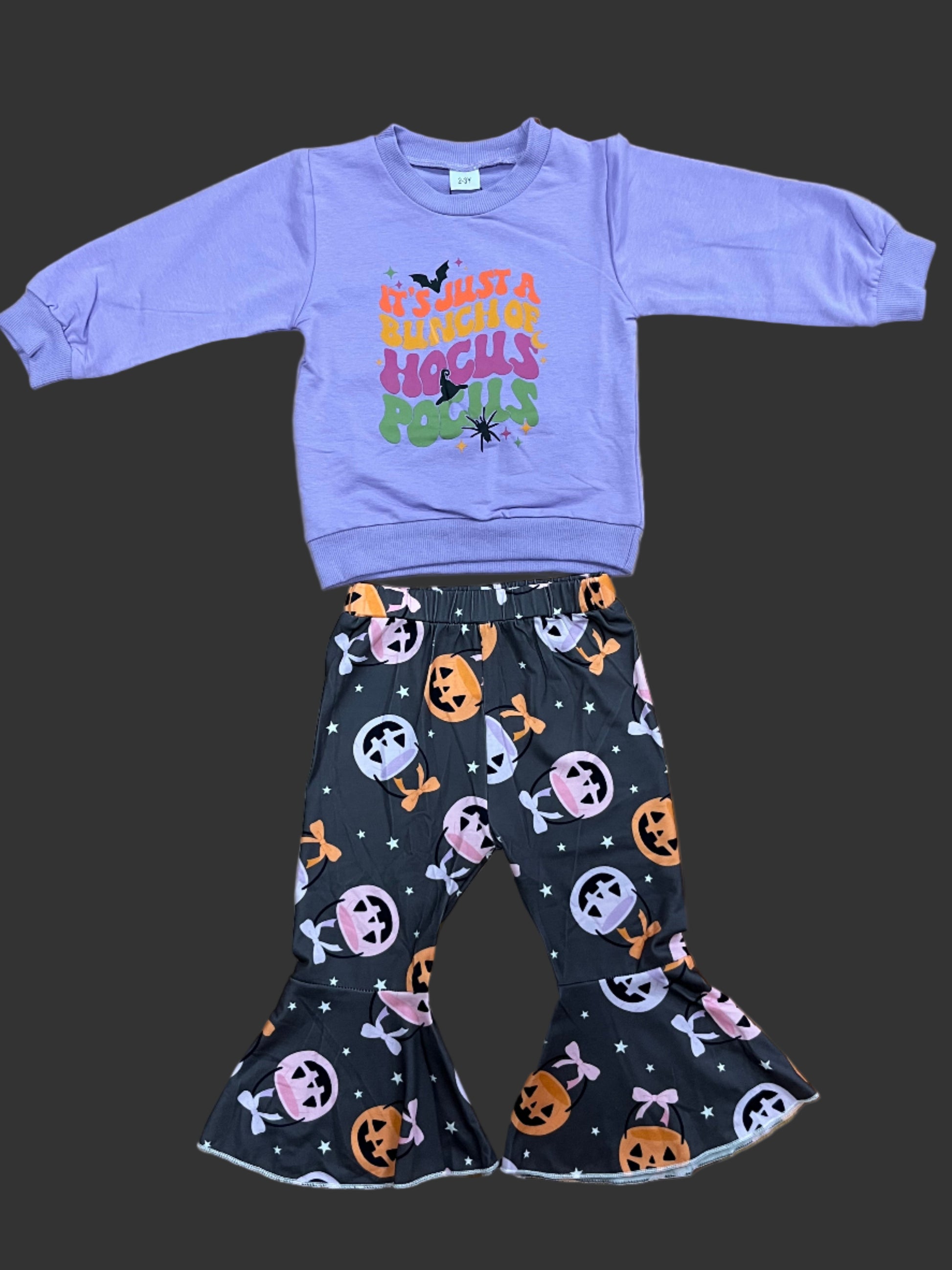 Purple long-sleeve shirt with colorful design and black Halloween-themed pants on a wooden surface